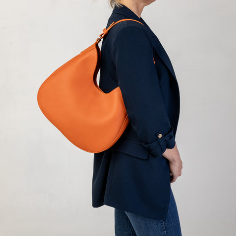 Cloe piccola, borsa da spalla in morbida pelle martellata arancio, design a sacca con accessori metallici color argento, firmata Pianigiani Bags.